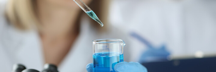 Female scientist dripping blue liquid from pipette into flask in laboratory