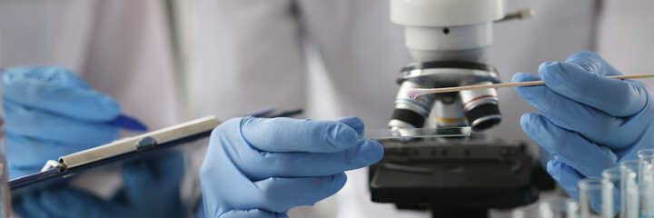 Scientists in protective gloves dripping liquid onto glass slide closeup