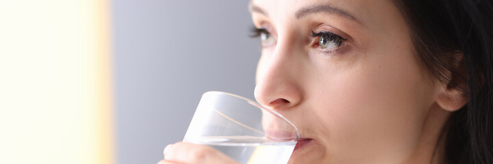 Young woman holding glass in her hands and drinking water from it