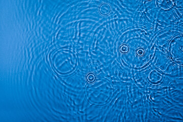 Fototapeta na wymiar De-focused transparent dark blue colored clear calm water surface texture with ripples, splashes and bubbles. Trendy abstract nature background. Water waves in sunlight with copy space.