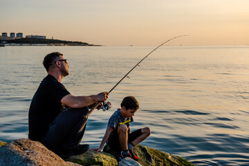 A fisherman sits on a rock by the sea with a fishing rod at sunset. Single sea fishing. Day at the...