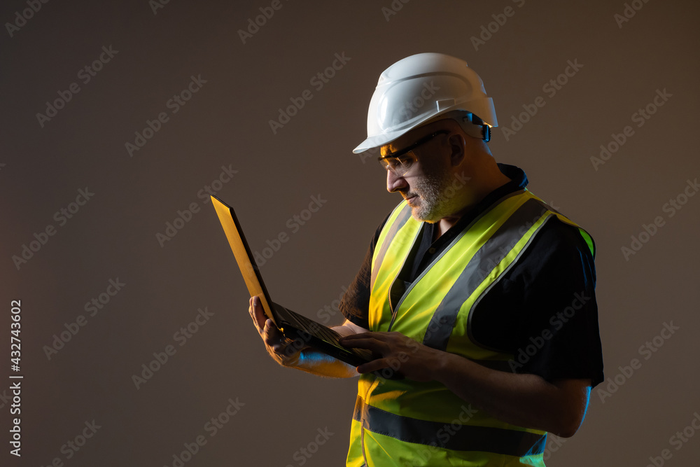 Poster builder in a helmet while working with a laptop. builder worker with a computer in hand. portrait of