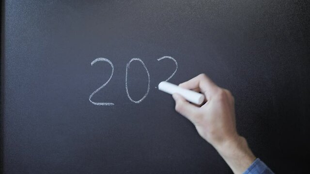 On chalkboard are drawn numbers 2021 and cross out. Writing 2021 on blackboard
