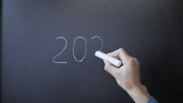 Hand erases from board 2021 and writing 2022 on blackboard with chalk