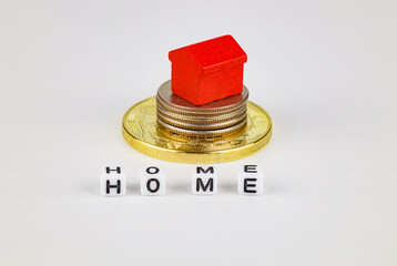 A toy red house stands on a stack of coins, a white background. Concept for buying, selling, renting, investing, home mortgages.