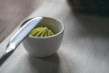 Bowl of green homemade butter with herbs and knife on white tablecloth on wooden table