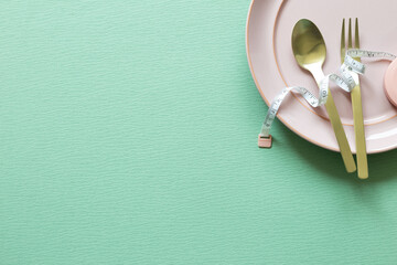 Plate and fork, spoon with measuring tape on green background. Diet concept