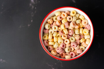 Cereal flakes in red bowl with copy space,Breakfast concept.Food with delicious fruity taste and fruity colours.It's made with maize,wheat,and barley. Cereal flakes in red bowl and dark backdrop.