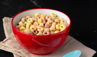 Cereal flakes in red bowl with copy space,Breakfast concept.Food with delicious fruity taste and fruity colours.It's made with maize,wheat,and barley. Cereal flakes in red bowl and dark backdrop.