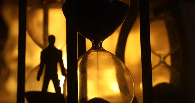 Time concept. Silhouette of a man standing between hourglasses with smoke and lights on a dark background. Surreal decorated picture