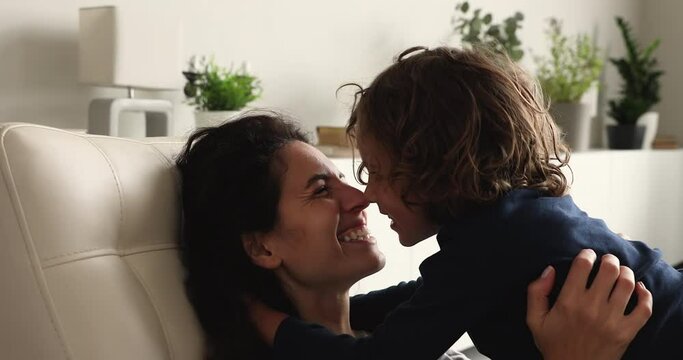 Head shot sincere beautiful hispanic latin woman touching noses with adorable preschool kid son, showing affectionate feelings to at home, relaxing together on comfortable sofa, happy family pastime.