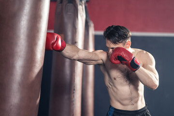 Caucasian male athlete punching heavy bag for boxer training in gym.