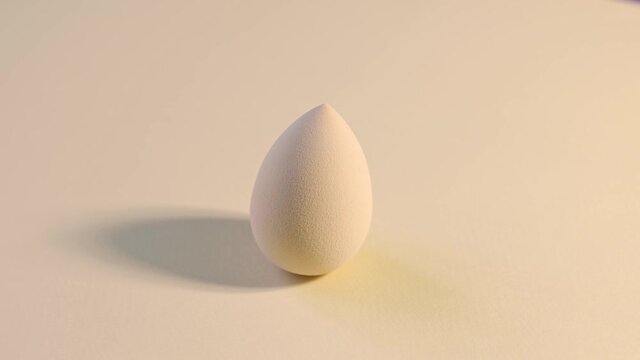 Cosmetic sponge beauty blender on a beige background rotating.