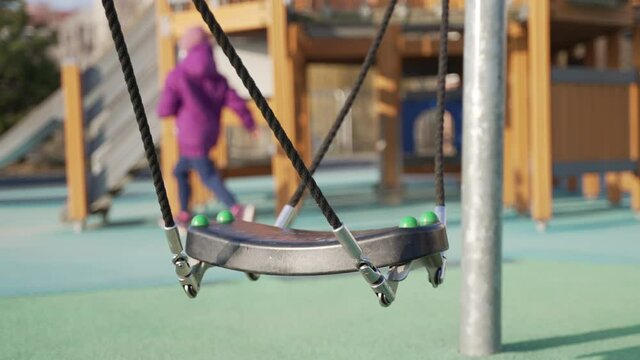 Closeup view of a rope swing in an outdoor playground. Kids running in the park and enjoying the swings. Concept of childhood carefree days. Wooden swing in the background. Bright sunny day. Winter