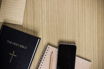 A mock up phone device with holy bible and notebook on table.