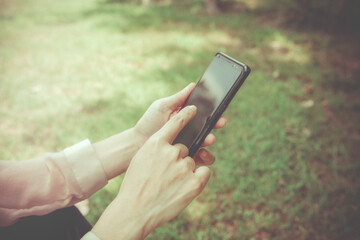 Smartphone Concept Everywhere, Woman uses her hand to touch the screen to search for messages or other information in the application while sitting on the green lawn.
