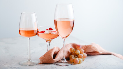 Rose wine in different types of glasses on light grey concrete background with grapes. Rose Wine composition on white table. Long web banner with copy space