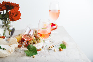 Rose wine in different wineglasses bottle on white table with grapes cheese, snacks bouquet of flowers. modern still life Rose Wine composition on light grey concrete background.