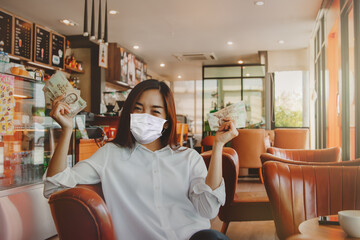 Happiness Beautiful woman sitting in a coffee shop wearing a mask, showing a five thousand baht...