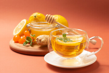 Ginger tea with mint and lemon. Healthy and hot drink. Liquid honey in honey-jar. Crystal cup on bright background. Selective focus.