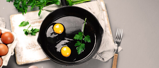Raw eggs in pan with herbs and seasoning on gray background, prepared food for breakfast.