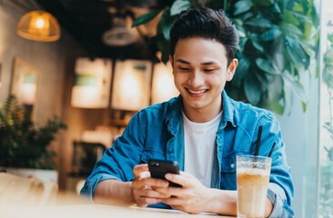 Young Asian man sitting and using smartphone at coffee shop - Powered by Adobe