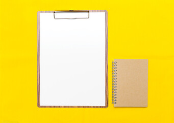 Wooden clipboard with blank paper white paper and notebook on yellow fabric background, blank paper sheet, office tool