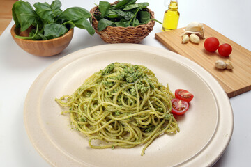 Asian style spaghetti with minced chicken spinach thai basil tomato garlic nutmeg olive oil presto sauce served on badge ceramic plate over on white background ingredients wooden board bowl
