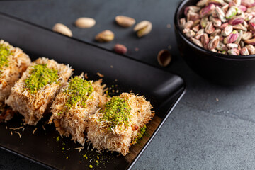Turkish tel kadayif dessert made from shredded phyllo dough mixed with walnuts. It is sweetened with thick syrup and ground pistachio is added on top for decoration and flavor. A plate with ingredient - obrazy, fototapety, plakaty