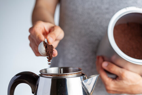 A caucasian woman is taking a teaspoon of ground coffee from a jar using a plastic measuring spoon and putting it into a percolator for brewing homemade morning coffee. Closeup selective focus image.