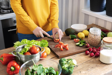 Young woman cuts vegetables to prepare delicious vegetarian or diet food in the home kitchen. Healthy lifestyle and wholesome food concept