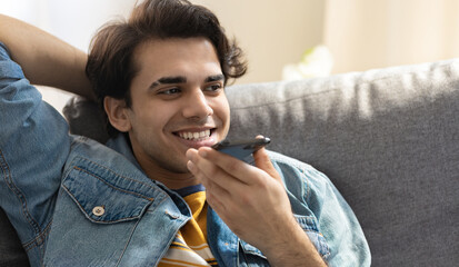 Happy young millennial caucasian man talking on the phone while sitting on the sofa at home. Home...