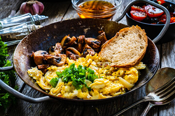 Delicious breakfast - scrambled eggs with fried white mushrooms and vegetable served on frying pan on wooden table
