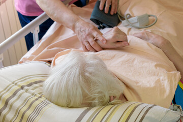 Checking the state of health of a bedridden patient. Woman lies in a medical bed. White hair....