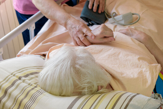 Checking The State Of Health Of A Bedridden Patient. Woman Lies In A Medical Bed. White Hair. Concept Of Caring For A Bedridden Patient With Dementia, Stroke.