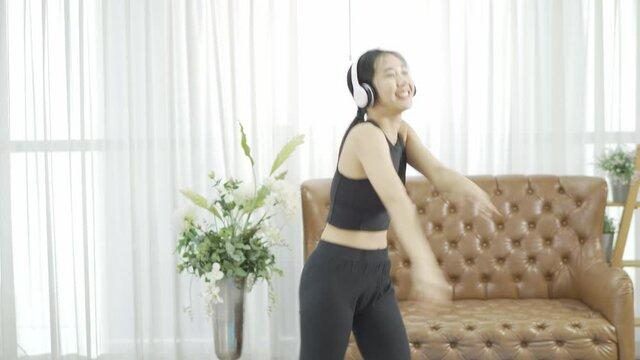 Asian female athletes wearing black sportswear, white headphones, exercise in yoga aerobics, background with sofa at home during new normalcy lifestyle.