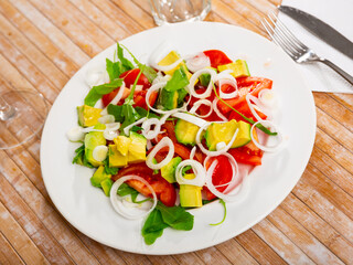 Organic mediterranean arugula salad with avocado and tomato on a plate in cafe