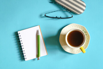 Notepad, eyeglasses and cup of coffee on blue color table top. Top view.