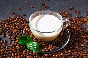 Cup of coffee on a gray table with coffee beans and coffee leaves. Closeup.