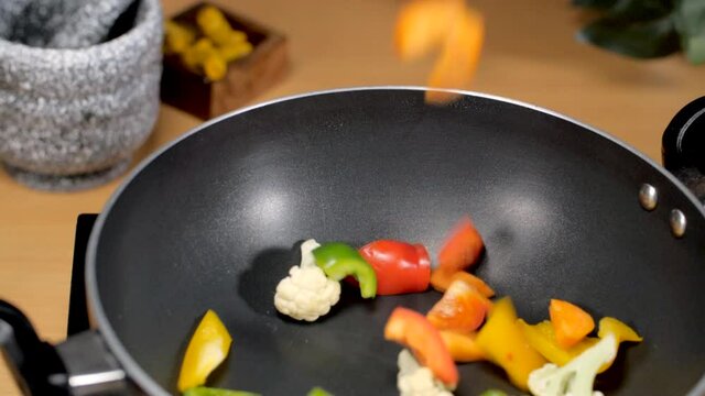 Closeup shot - Making of the colorful vegetable dish/recipe in the home kitchen. Modern kitchen scene of chef cooking mixed vegetables in a nonstick pan on an induction cooker - food concept