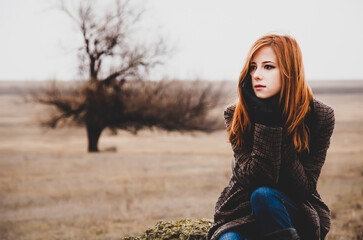 Redhead girl sitting at outdoor in autumn time.