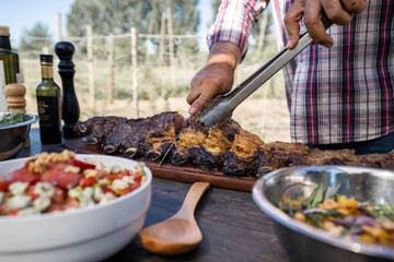 man cutting roast beef on a table with salads