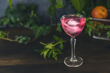 Elegant stemware glass of blood orange cocktail with big ice ball on dark wooden table surface
