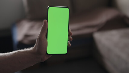 Man use smartphone with green screen while standing in living room