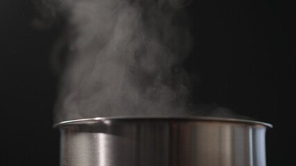 Fototapeta na wymiar Steam rising from pot over black background