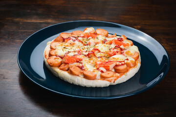 Pizza, sausage and crab sticks in a ceramic plate on a wooden table.