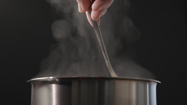 man hand stiring with fork in pot with rising steam