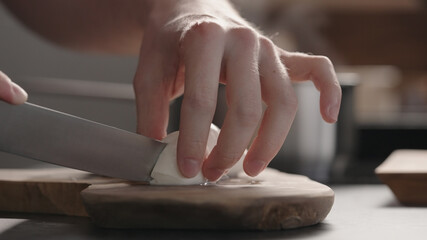 man slicing medium sized mozzarella balls with knife on olive wood board