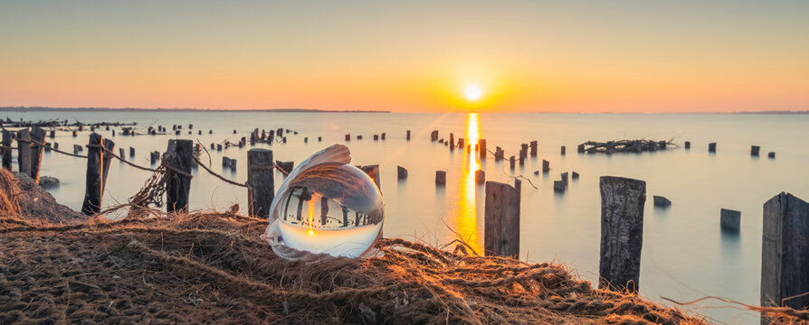 Vue d'une boule de cristal dans un coquillage sur un filet de pêcheur avec un coucher de soleil sur un étang de la Camargue, réserve naturelle protégée.	