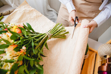 A florist cuts packaging paper with scissors on a desktop in a flower shop. On the paper is a bouquet of fresh flowers